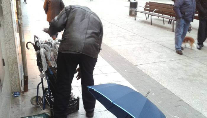 Un vendedor ambulante co seu carro de paraugas nunha rúa do centro da Coruña este venres